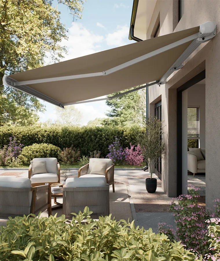 Store banne taupe déployé au-dessus d’une terrasse de maison, protégeant deux fauteuils de jardin de la lumière directe